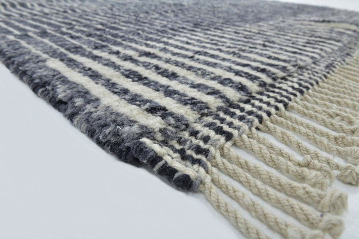 Close-up detail of a black and white rug featuring a striped pattern and fringe edges.