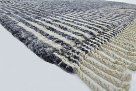 Close-up detail of a black and white rug featuring a striped pattern and fringe edges.