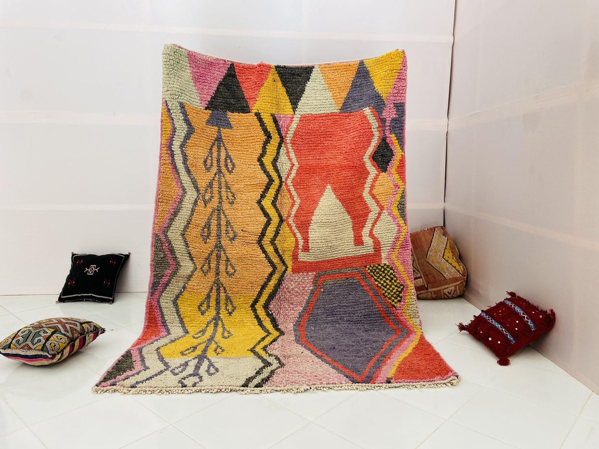 Lifestyle shot of the orange and pink abstract Moroccan rug with geometric patterns on a white background.