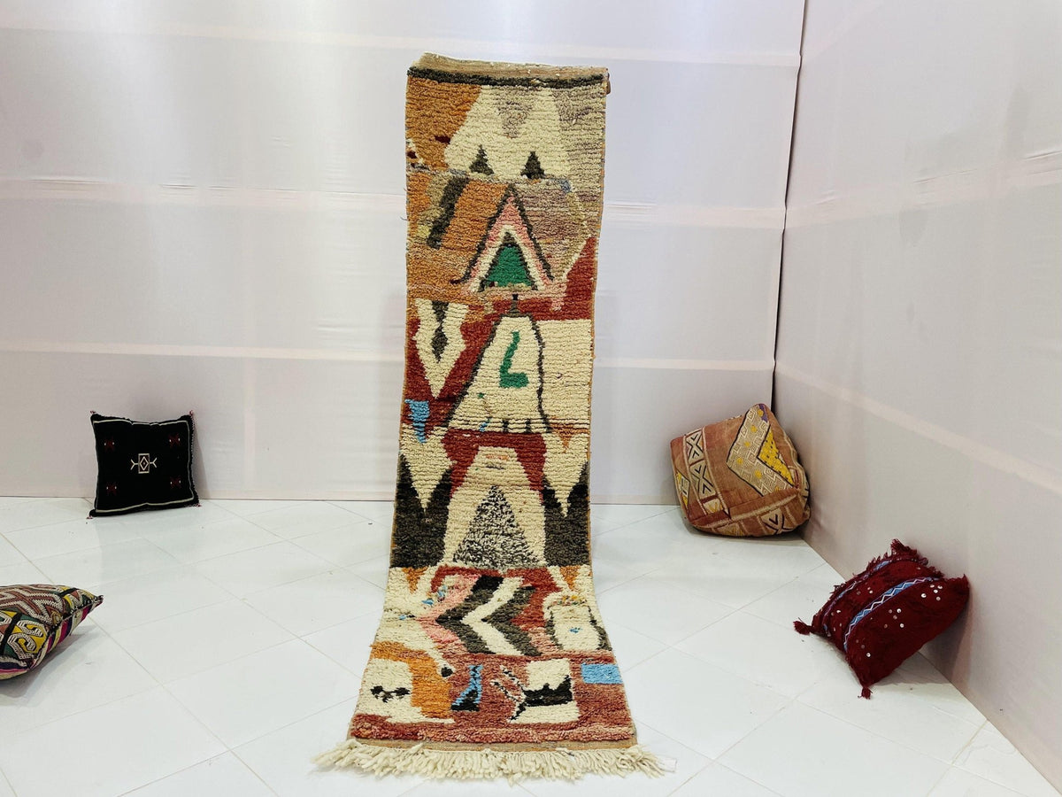 Lifestyle shot of a vintage Moroccan runner rug featuring geometric patterns in cream, red, green, and black.