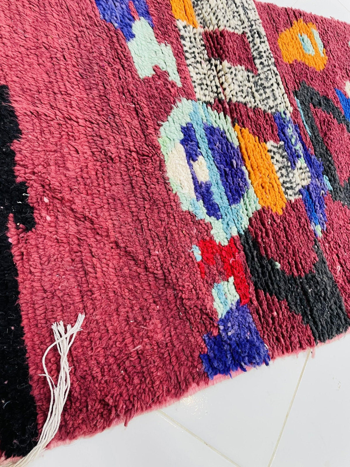 Side view of a vintage Moroccan rug featuring geometric shapes in red, blue, orange, and black.