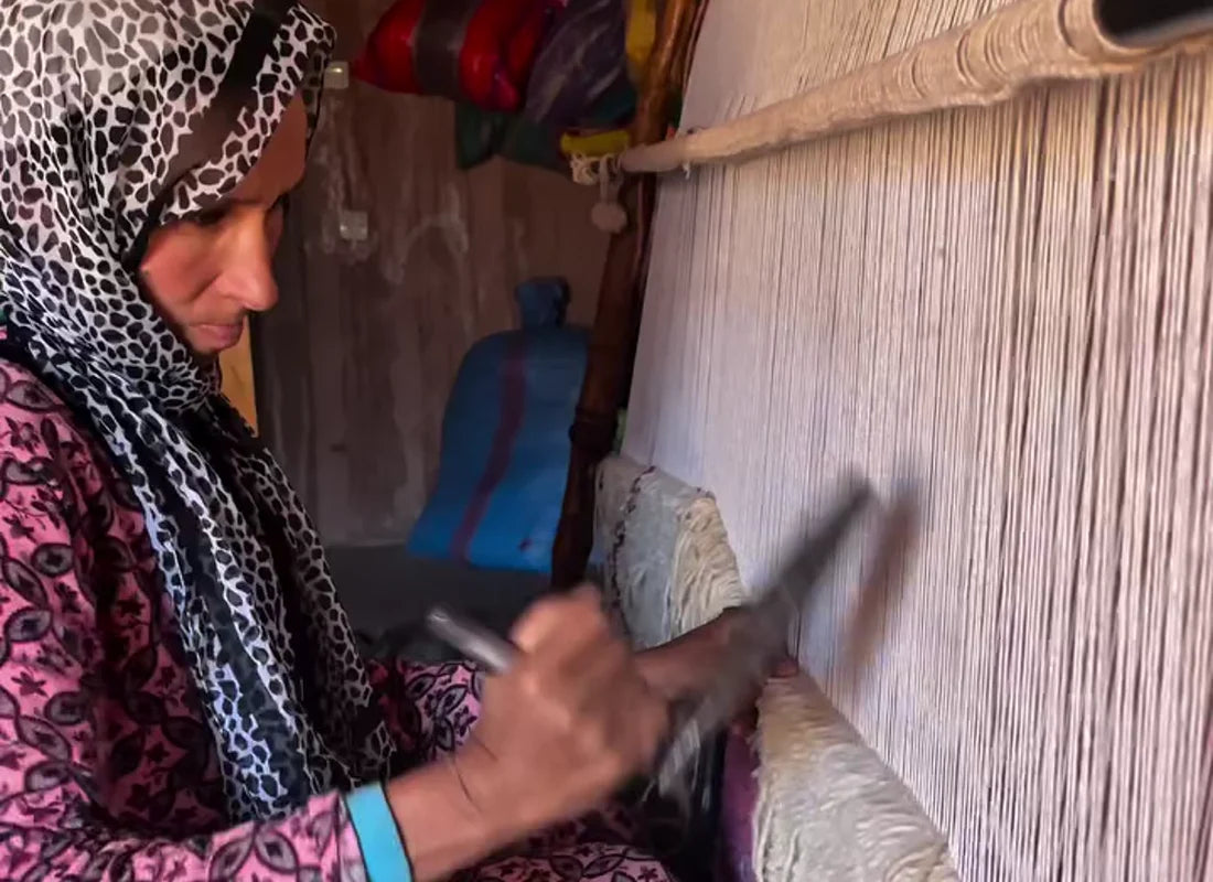A Moroccan artisan handweaving a wool rug on a traditional loom